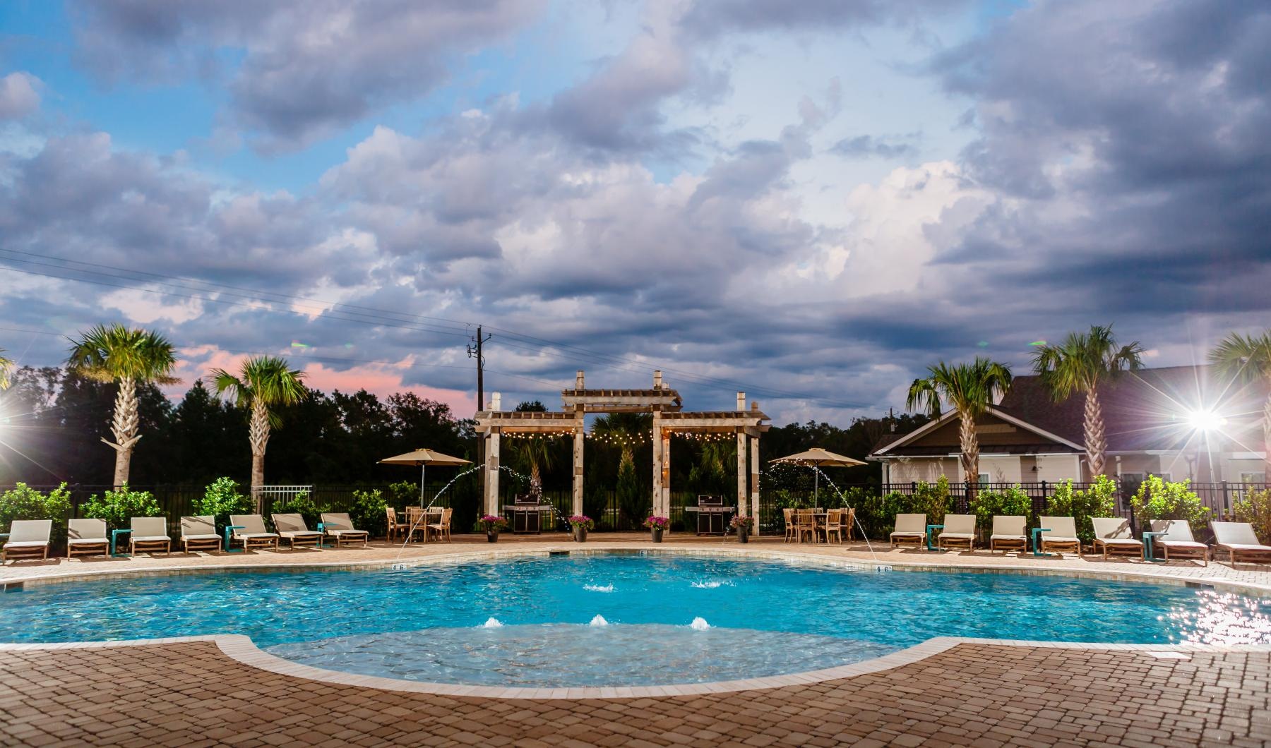 a pool with lounge chairs and umbrellas by a building with palm trees